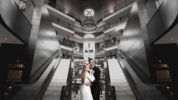 Una pareja en una escalera mecánica dentro de un edificio moderno con un diseño geométrico, que incluye un candelabro central y señalización de marca.