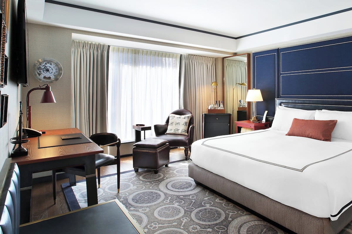 Una habitación de hotel con una cama grande, un escritorio, una silla, una mesita y una lámpara.