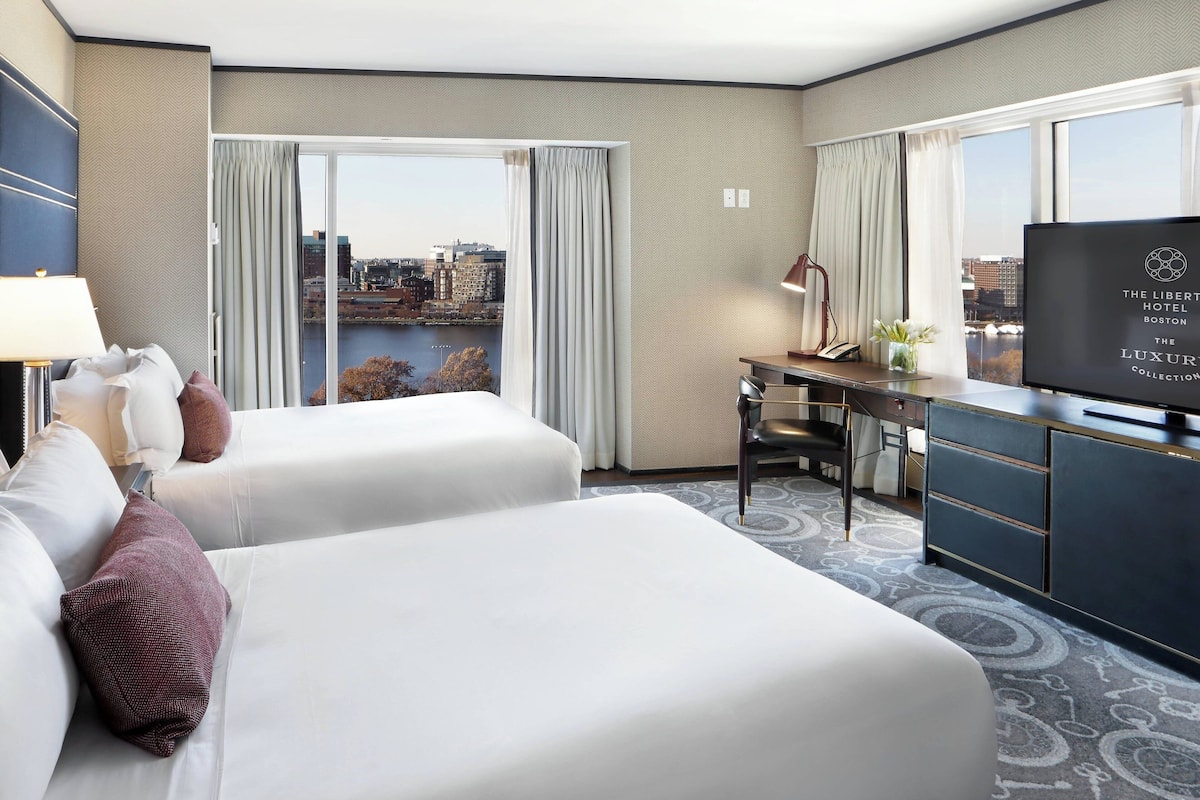 Habitación de hotel con dos camas, un escritorio, un televisor y vista a la ciudad.