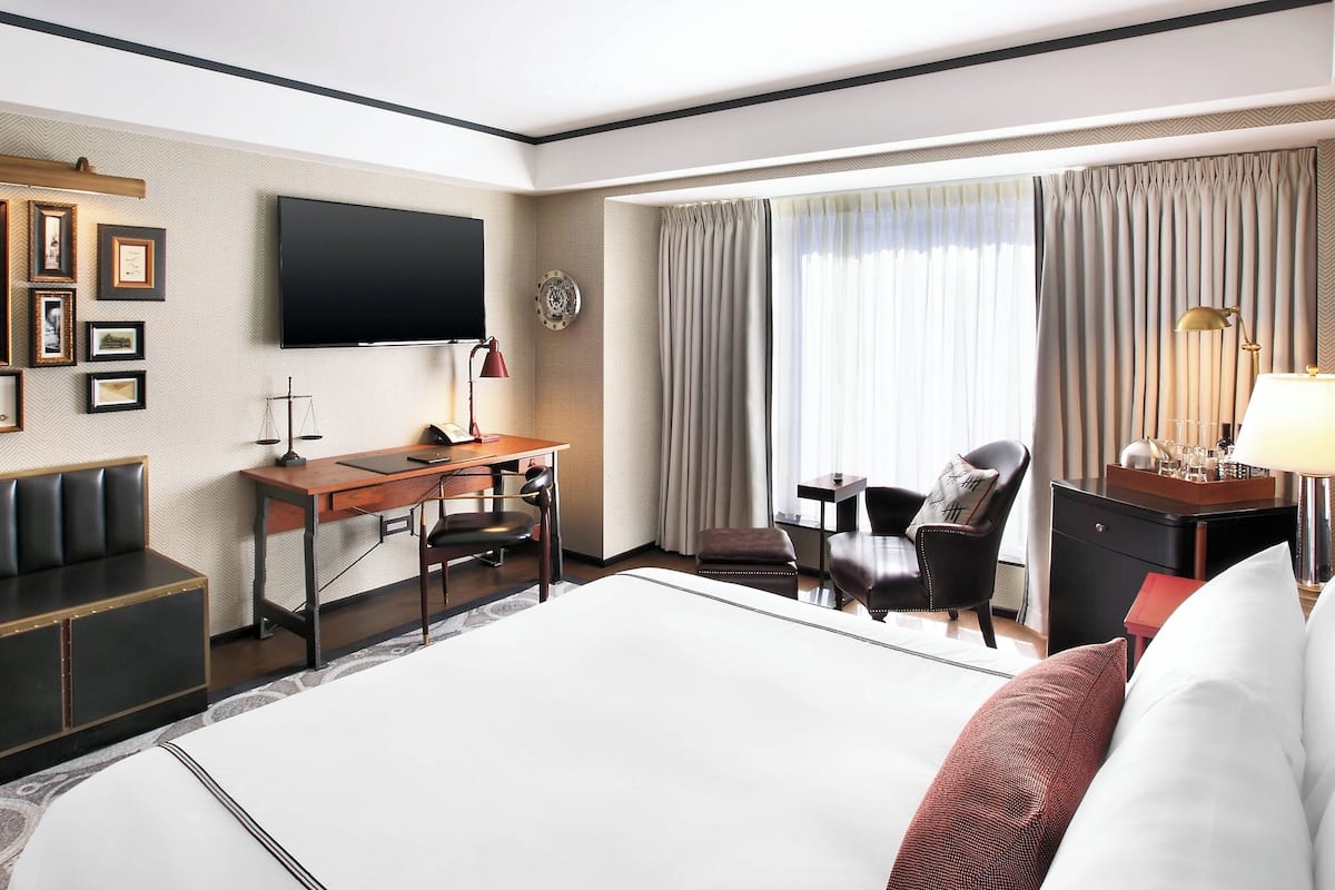 Habitación de hotel con una cama grande, un escritorio, una silla, un televisor y vistas al exterior a través de la ventana.