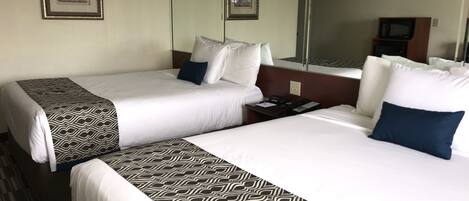 A hotel room with two beds, each with a patterned bedspread, white bedding, and a nightstand with a phone and a lamp.