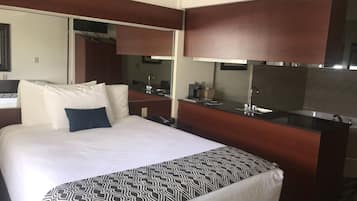 Una habitación de hotel con una cama grande, un escritorio empotrado, un espejo y una kitchenette.