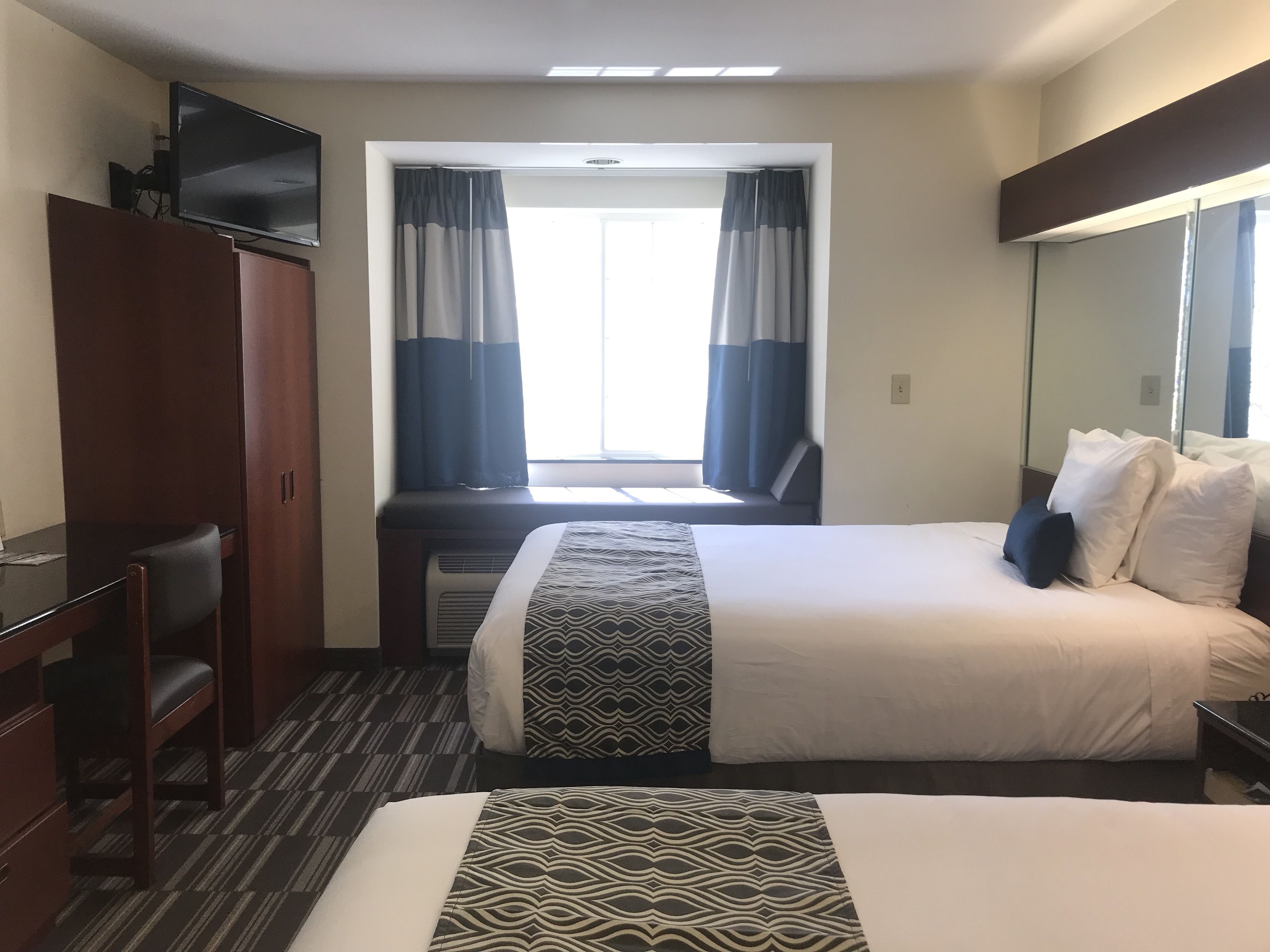 A hotel room with a bed, a desk, a chair, a wardrobe, and a television.