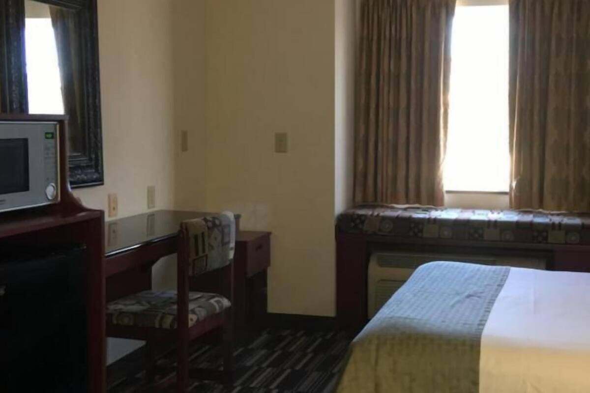 Una camera d'albergo con un letto, una scrivania con una sedia, una televisione e una finestra con tende.