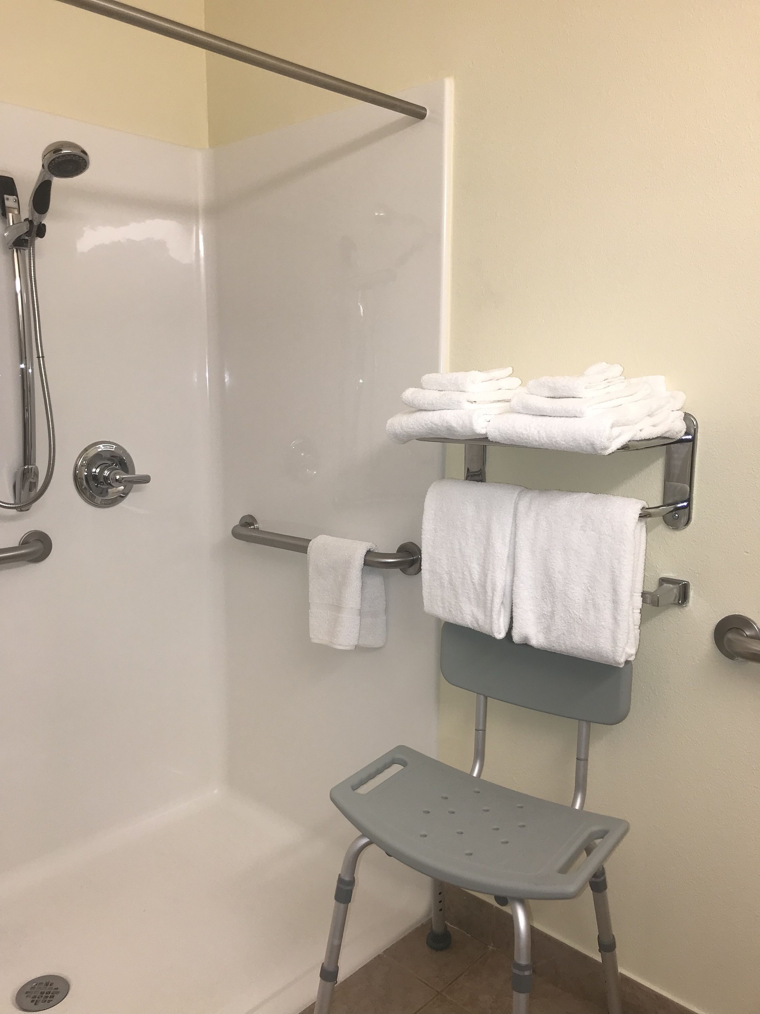 A shower area with a grab bar, a towel rack with folded towels, and a shower seat.