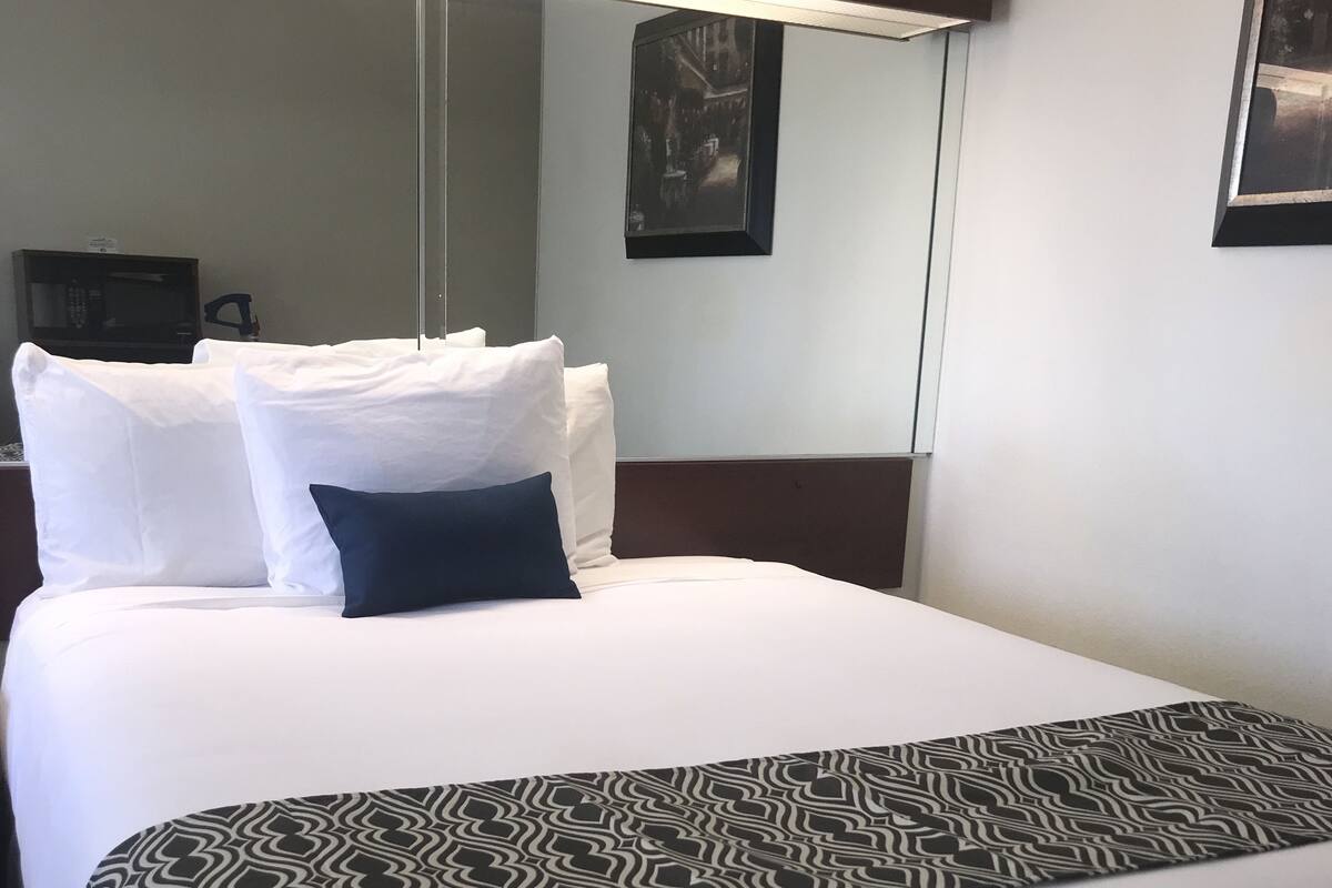 Camera d'albergo con un letto grande, biancheria da letto bianca, una coperta decorata e una TV a schermo piatto montata a parete.
