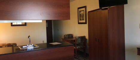 Una habitación de hotel con cama, kitchenette, televisor y armario.