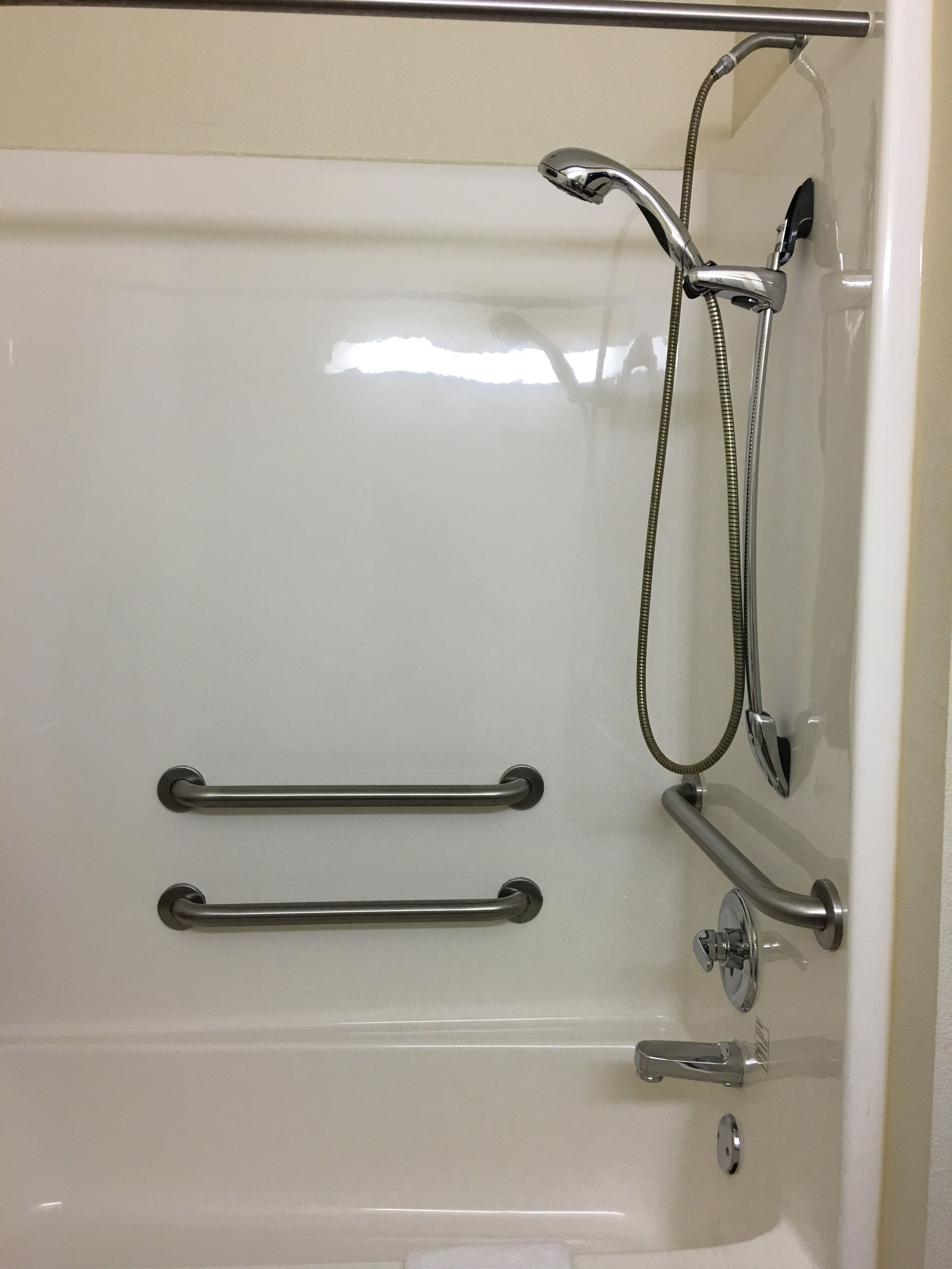 A bathroom with a bathtub, grab bars, a shower head, and a handheld shower attachment.