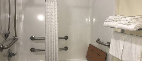 A walk-in shower with a glass door, a towel rack with folded towels, and a wooden panel on the wall.