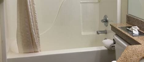 Un baño moderno con ducha de vidrio, inodoro blanco y encimera de granito con espejo.