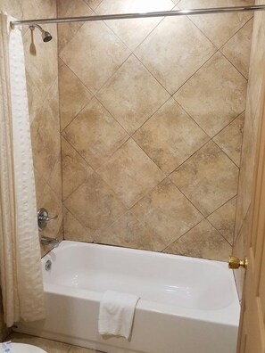 A bathroom with a bathtub, a showerhead, and a towel hanging on the wall.