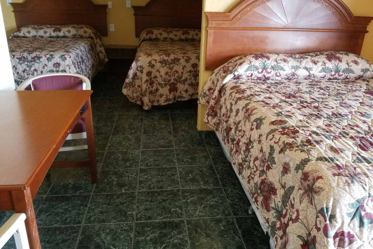 A hotel room with three beds, a wooden desk, and a chair.