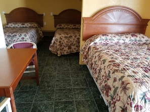 A hotel room with three beds, a wooden desk, and a chair.
