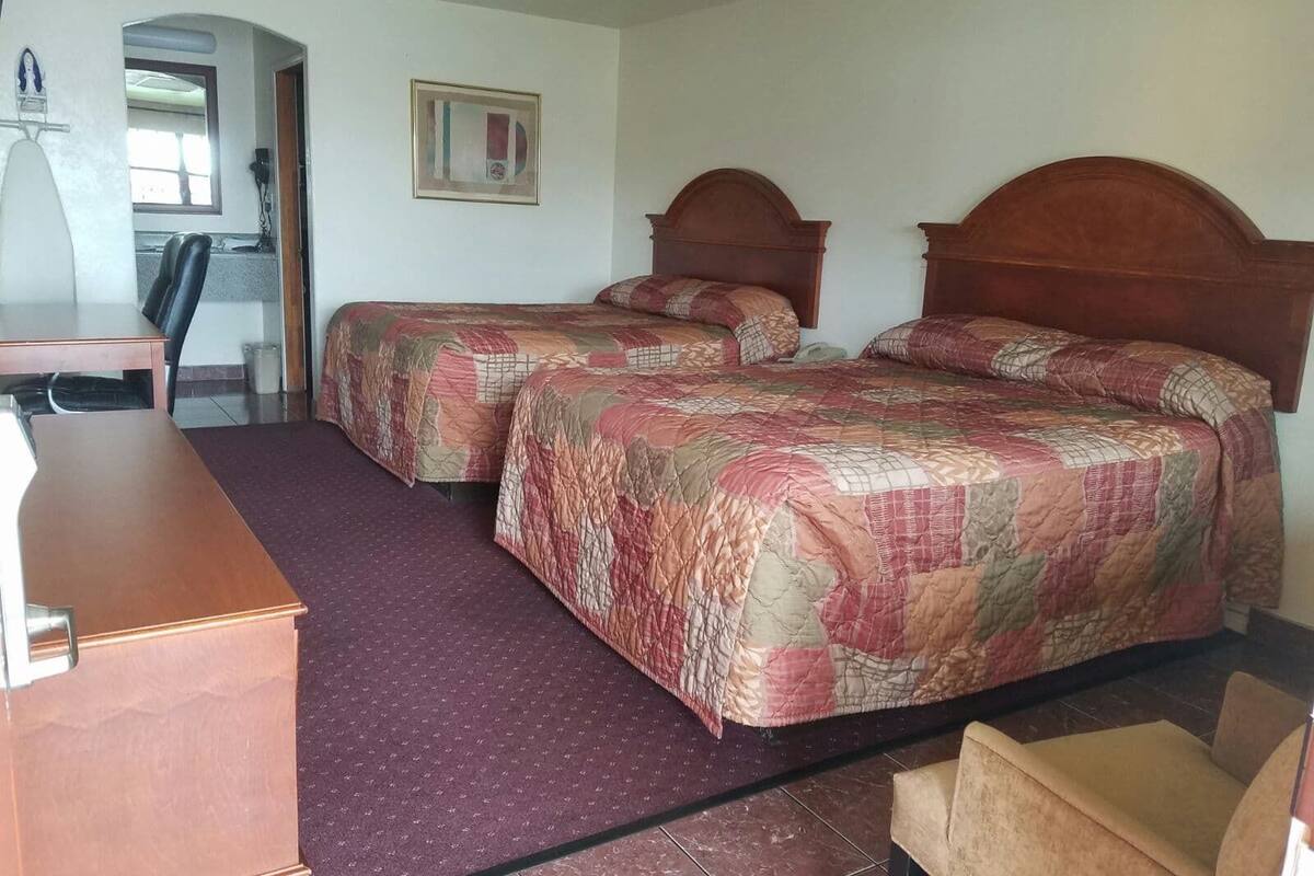 A hotel room with two beds, a desk, and a chair.