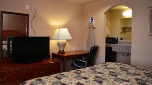 Ein Hotelzimmer mit einem Bett, einem Schreibtisch mit Lampe, einem Fernseher, einem Sessel und einer Mikrowelle.