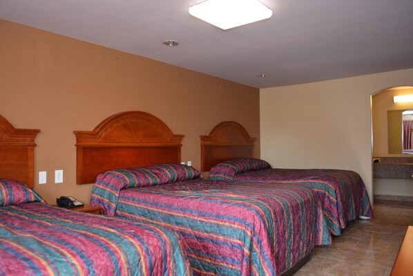 A hotel room with three beds, each with a wooden headboard, and a small bedside table with a phone. - El Camino Motel (Beeville)