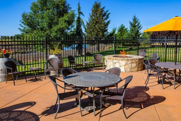 An outdoor patio area with a round metal table and chairs, a stone fire pit, and a yellow umbrella. - Comfort Inn & Suites Walla Walla (Walla Walla)