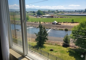 A view from a window overlooking a river with a small dock, a fenced area with trees, and distant buildings. - Comfort Inn & Suites Walla Walla (Walla Walla)