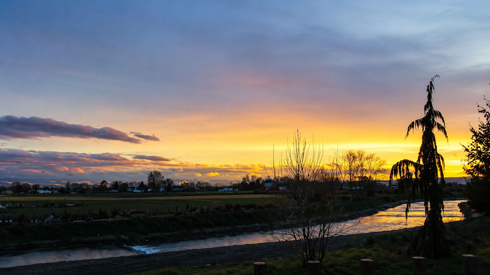 Un paysage rural avec une rivière, des arbres et un coucher de soleil.