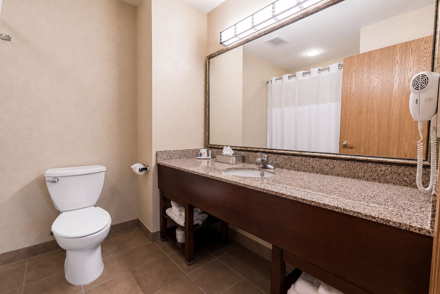A bathroom with a toilet, sink, mirror, and hairdryer.