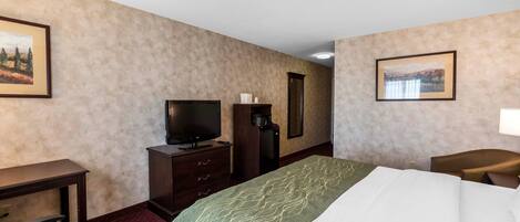 A hotel room with a bed, a desk, a television, a coffee machine, and two framed pictures on the walls.