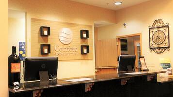 A hotel reception desk with a sign reading "Comfort Inn & Suites," a clock, and a security camera.