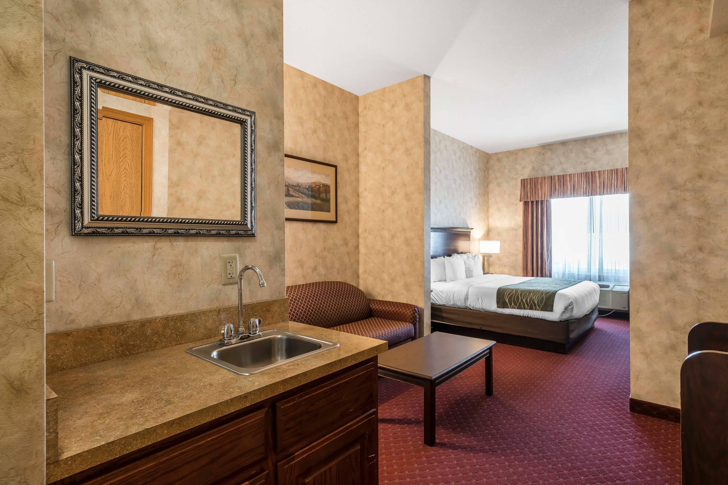 Une chambre d’hôtel équipée d’une kitchenette, d’un lit, d’un canapé et d’une grande fenêtre avec des rideaux.
