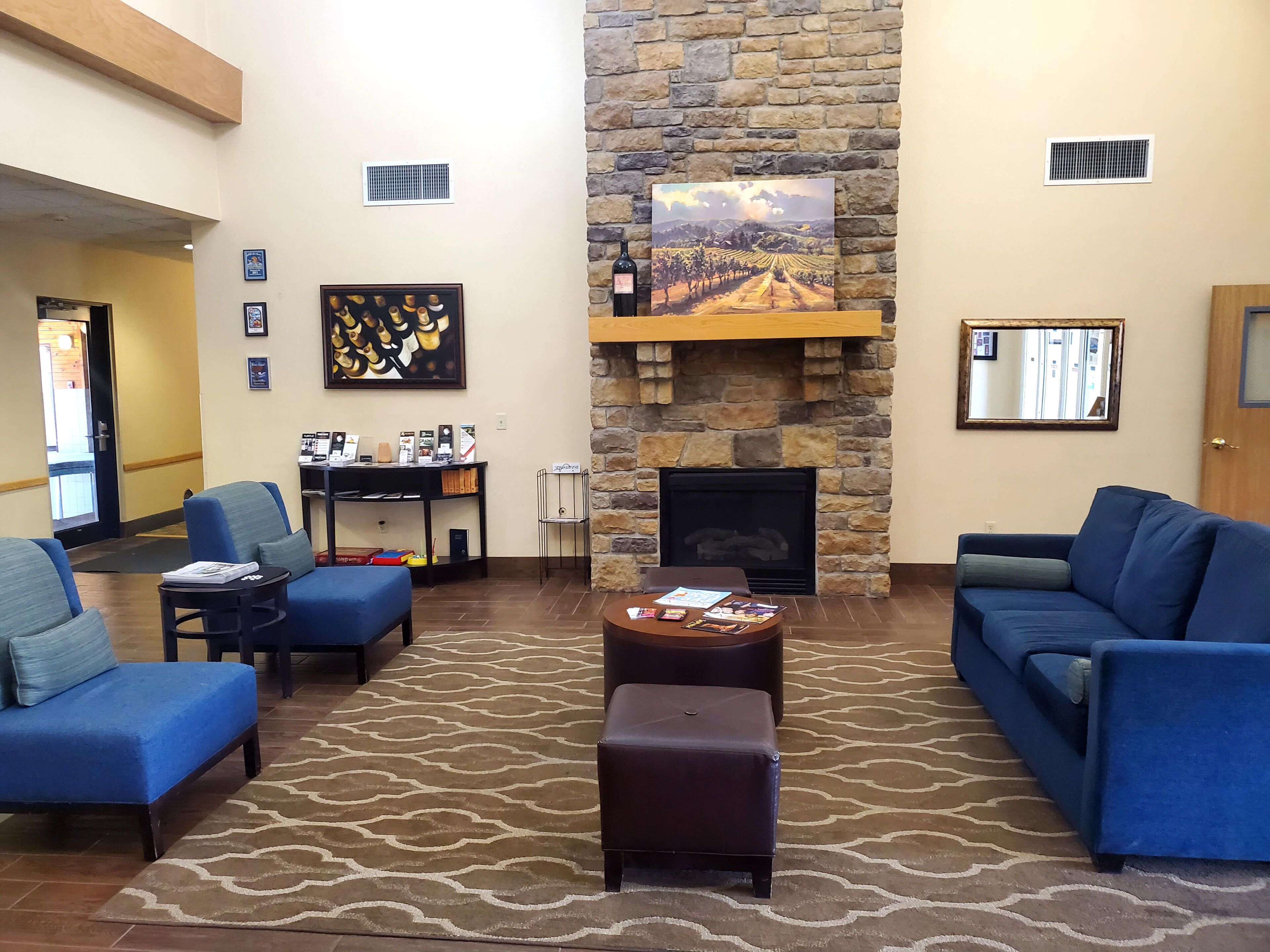 A hotel lobby with a stone fireplace, blue sofas, a coffee table, and a carpeted floor.