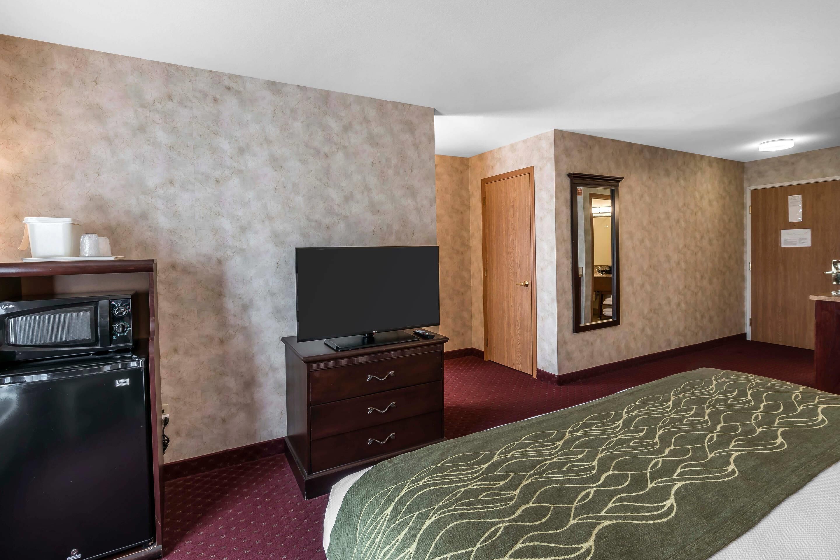 A hotel room with a bed, a dresser with a flat-screen TV, a microwave, and a refrigerator.