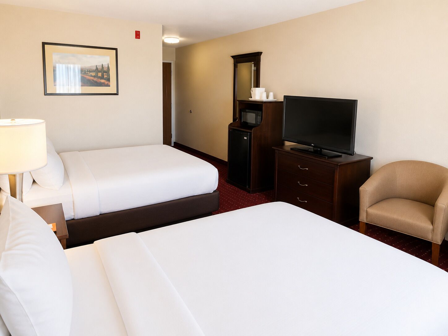 A hotel room with two beds, a television, a desk with a microwave, a chair, and a framed picture on the wall.