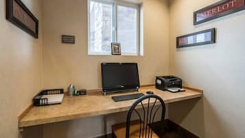 Un escritorio pequeño con una computadora, una impresora y una silla. Hay una ventana y, sobre el escritorio, un cuadro en la pared.
