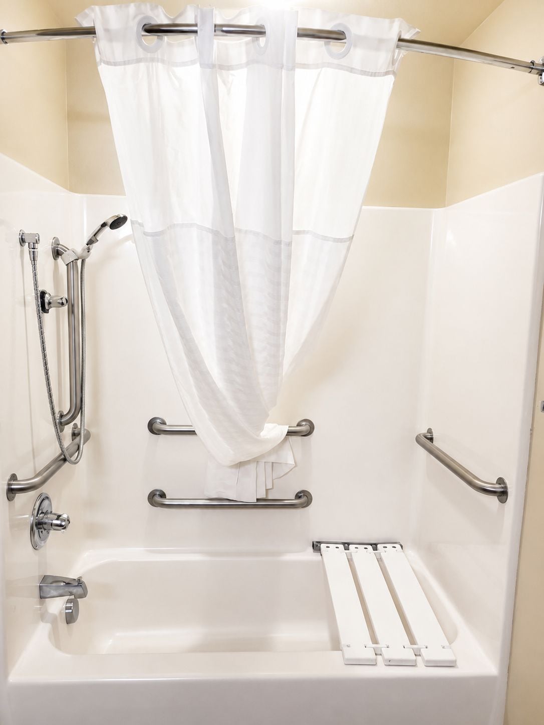 A bathroom with a shower, grab bars, and a white bathtub.