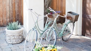 Una veranda coperta con due biciclette parcheggiate sotto una trave in legno, una pianta in vaso con fiori e un recinto di legno sullo sfondo.