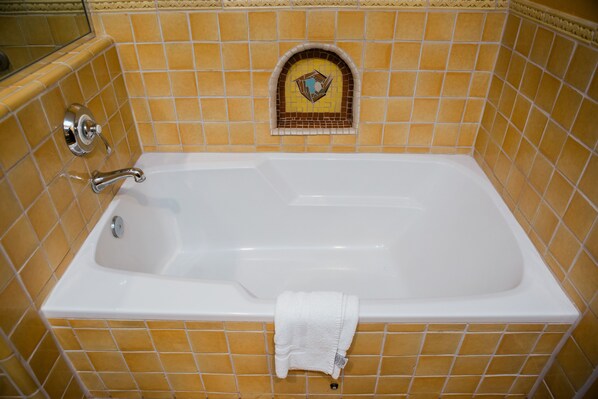 Una bañera con una toalla blanca colgada al lado, rodeada de paredes con azulejos amarillos y un azulejo decorativo sobre la bañera.