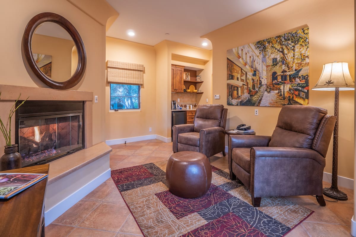 A living room with a fireplace, leather chairs, a patterned rug, and a painting on the wall.