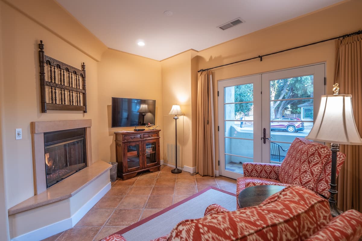 A living room with a fireplace, a television, a sofa, and a view of the outside through a glass door.