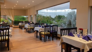 A restaurant with multiple tables, chairs, and a large window offering a view of greenery and a building. - Swiss Inn Pyramids Golf Resort (6th of October City)
