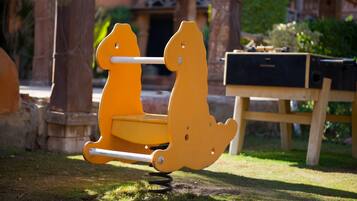 Kids can play on this dinosaur-shaped swing set, surrounded by trees and a nearby bench.