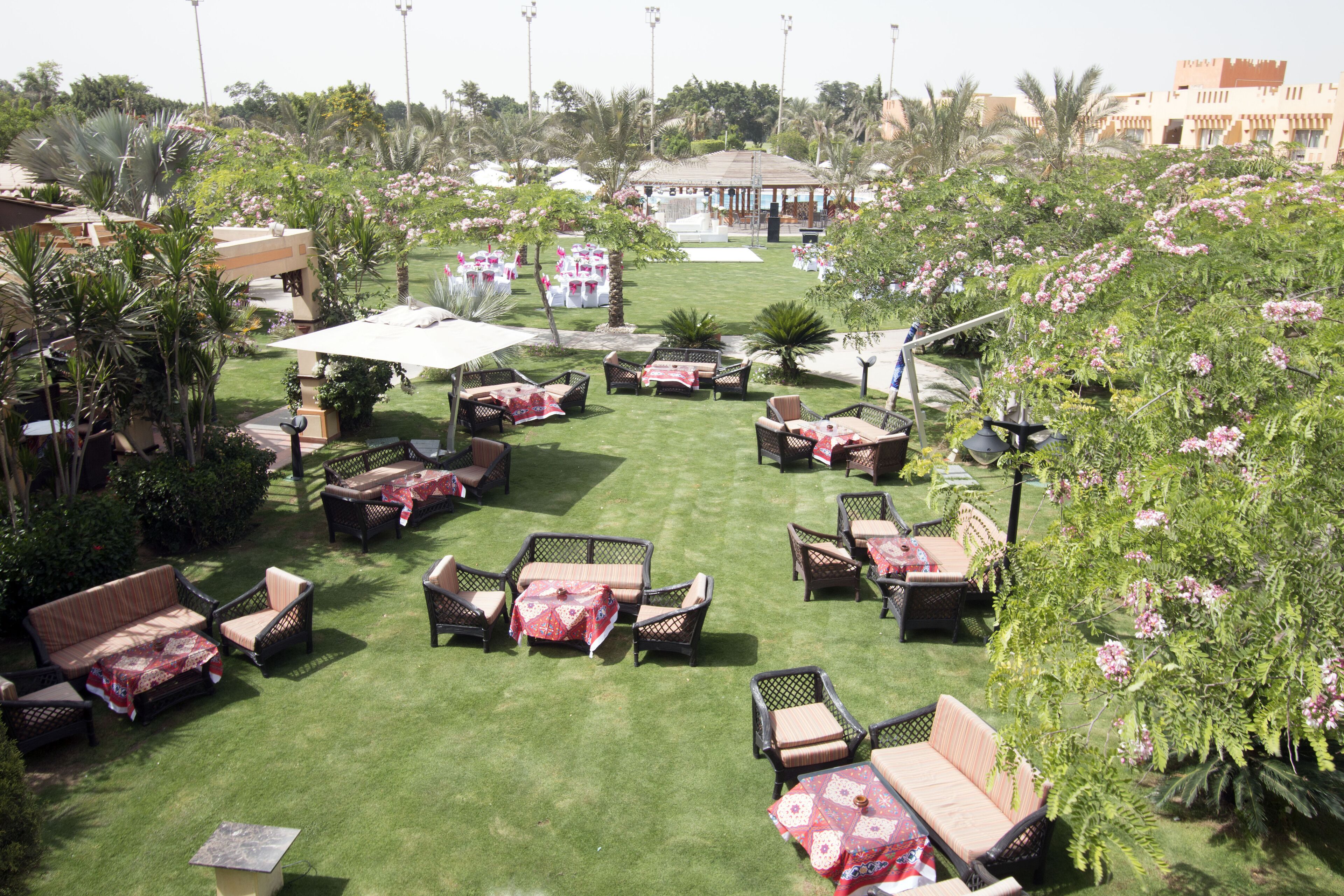 An outdoor seating area with multiple tables and chairs, surrounded by lush greenery and flowering plants.
