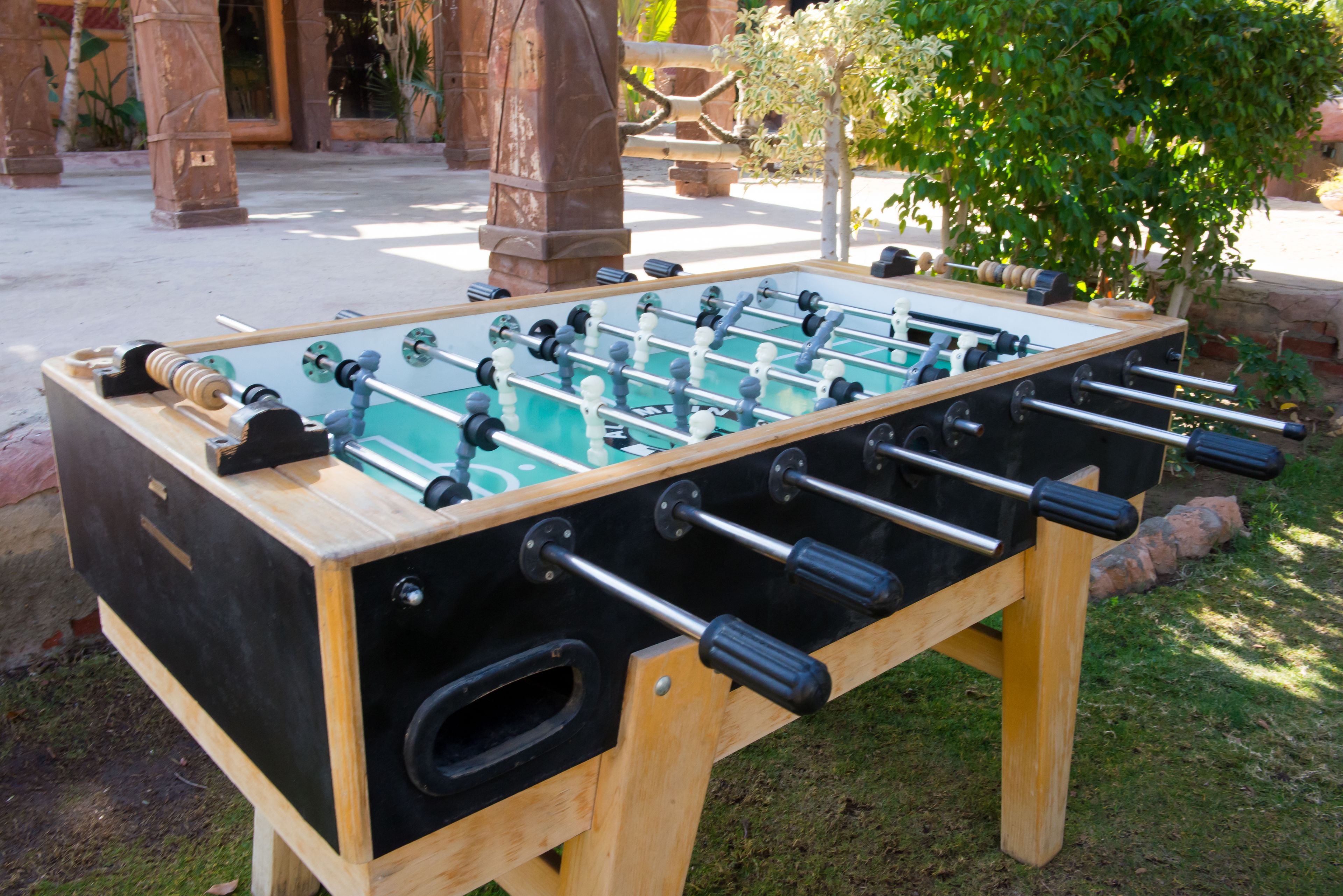 A wooden foosball table with black and white balls, set outdoors on a grassy area.