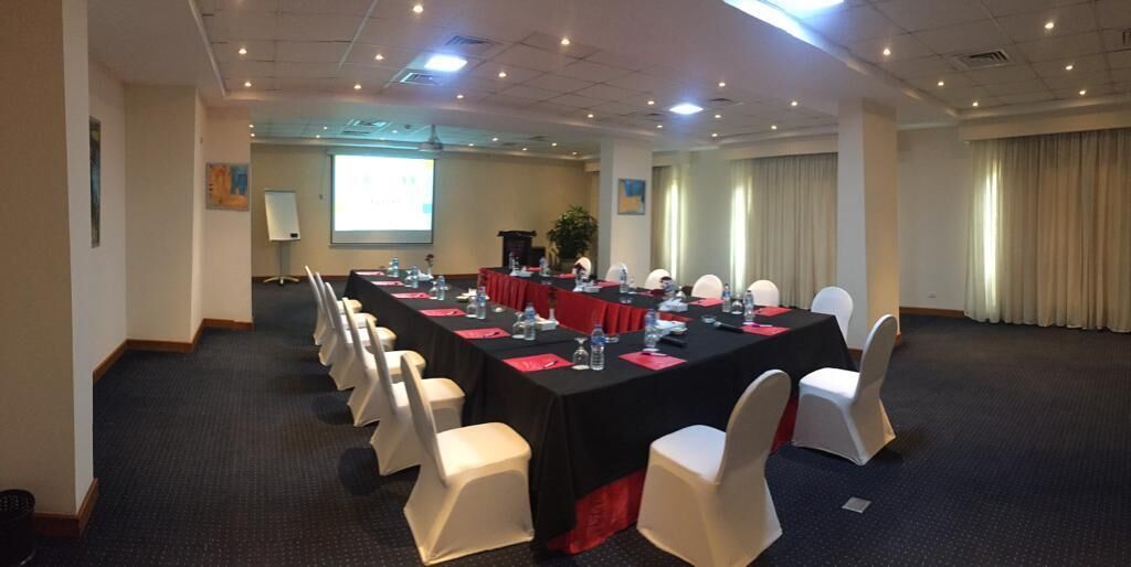 A conference room with a long table, white chairs, and a projector screen.