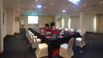 A conference room with a long table, white chairs, and a projector screen.
