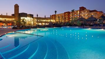 A large indoor swimming pool with clear water, surrounded by a hotel with multiple balconies and a rock formation.