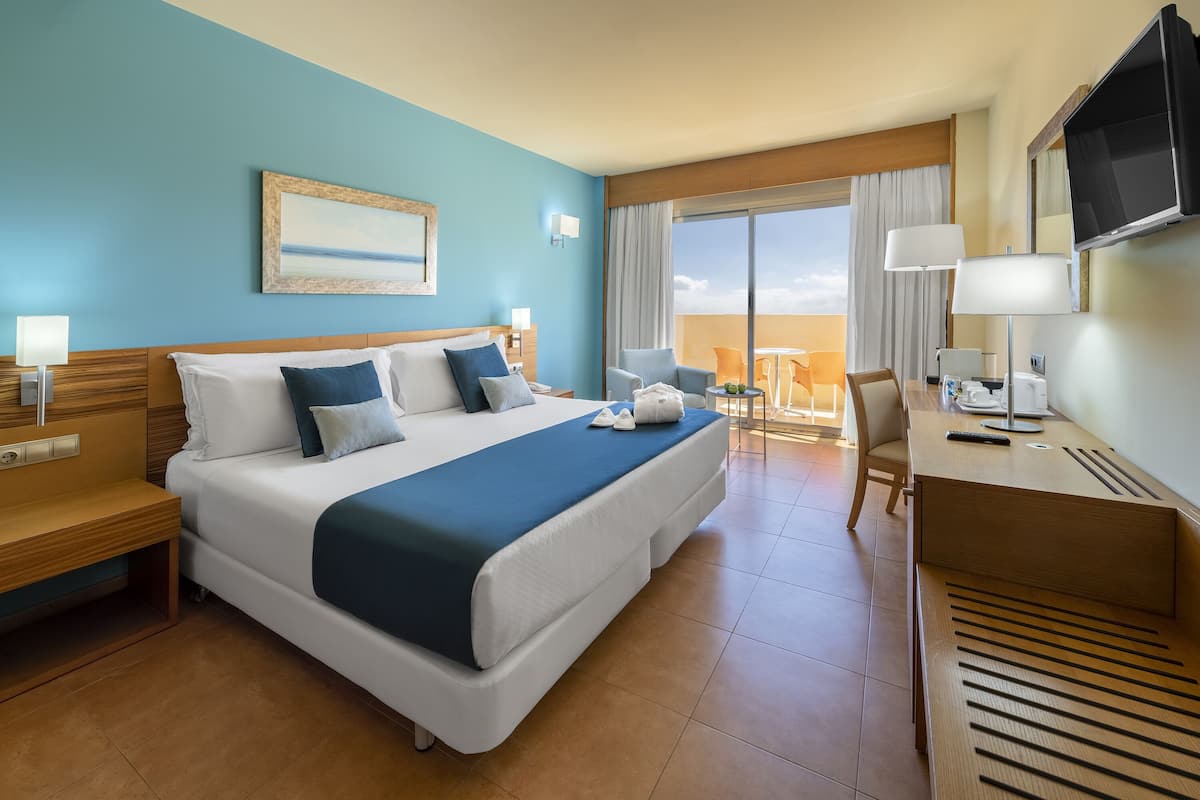 Ein Hotelzimmer mit einem großen Bett, einem Schreibtisch, einem Stuhl und einem Balkon mit Blick.