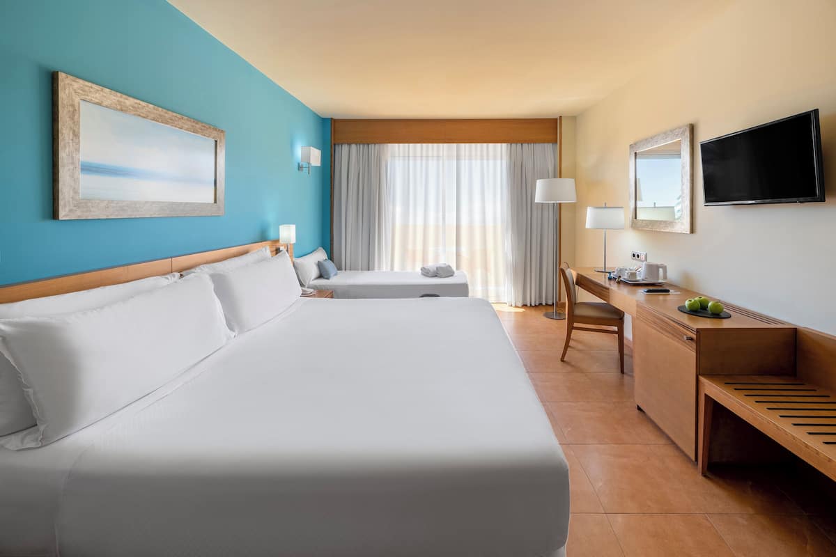 Ein Hotelzimmer mit zwei Betten, einem Schreibtisch, einem Stuhl, einem Fernseher und einem Fenster mit Vorhängen.