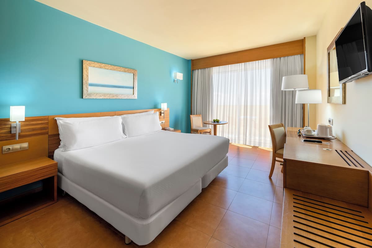 Ein Hotelzimmer mit Bett, Schreibtisch, Stuhl, Fernseher und einem Bild an der Wand.