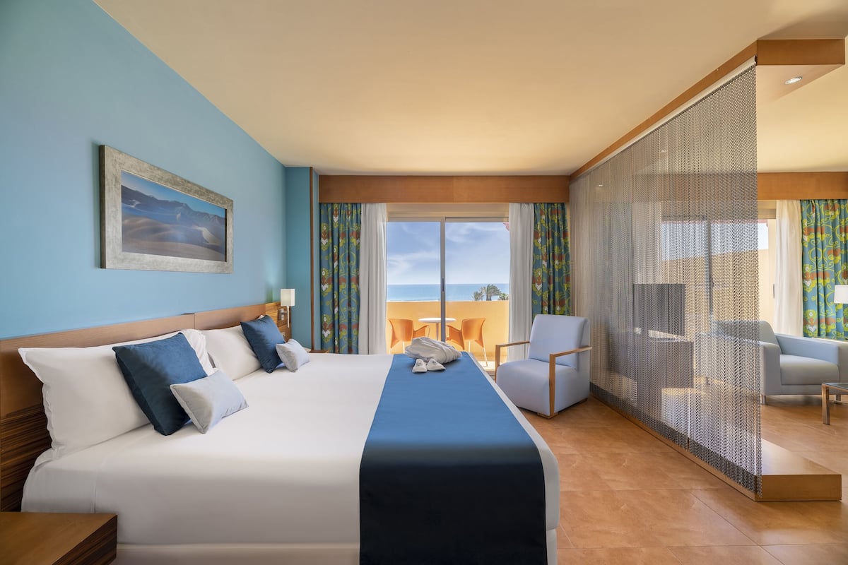 A hotel room with a bed, a desk, a chair, and a view of the ocean.