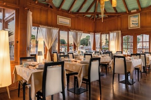 Un restaurante con varias mesas dispuestas para comer, paredes de madera y grandes ventanales.