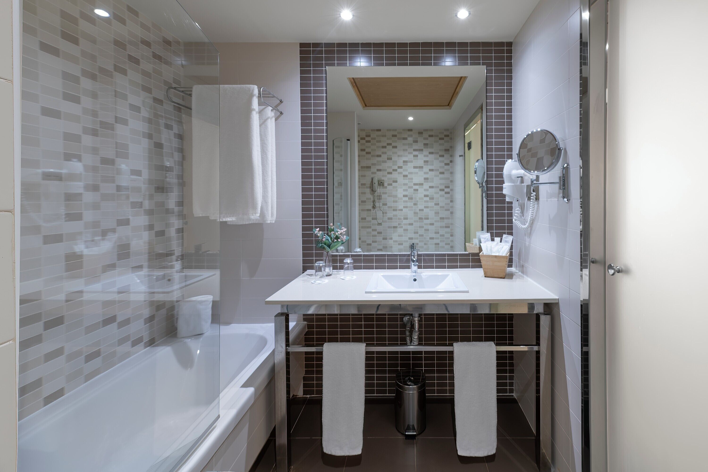 Un baño moderno con bañera, lavamanos y ducha. Hay toallas colgadas en la pared y un cesto de basura debajo del lavamanos.