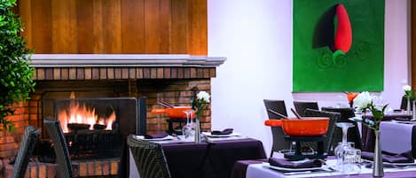 Un restaurante con chimenea de ladrillo, sillas de mimbre y un cuadro abstracto verde en la pared.